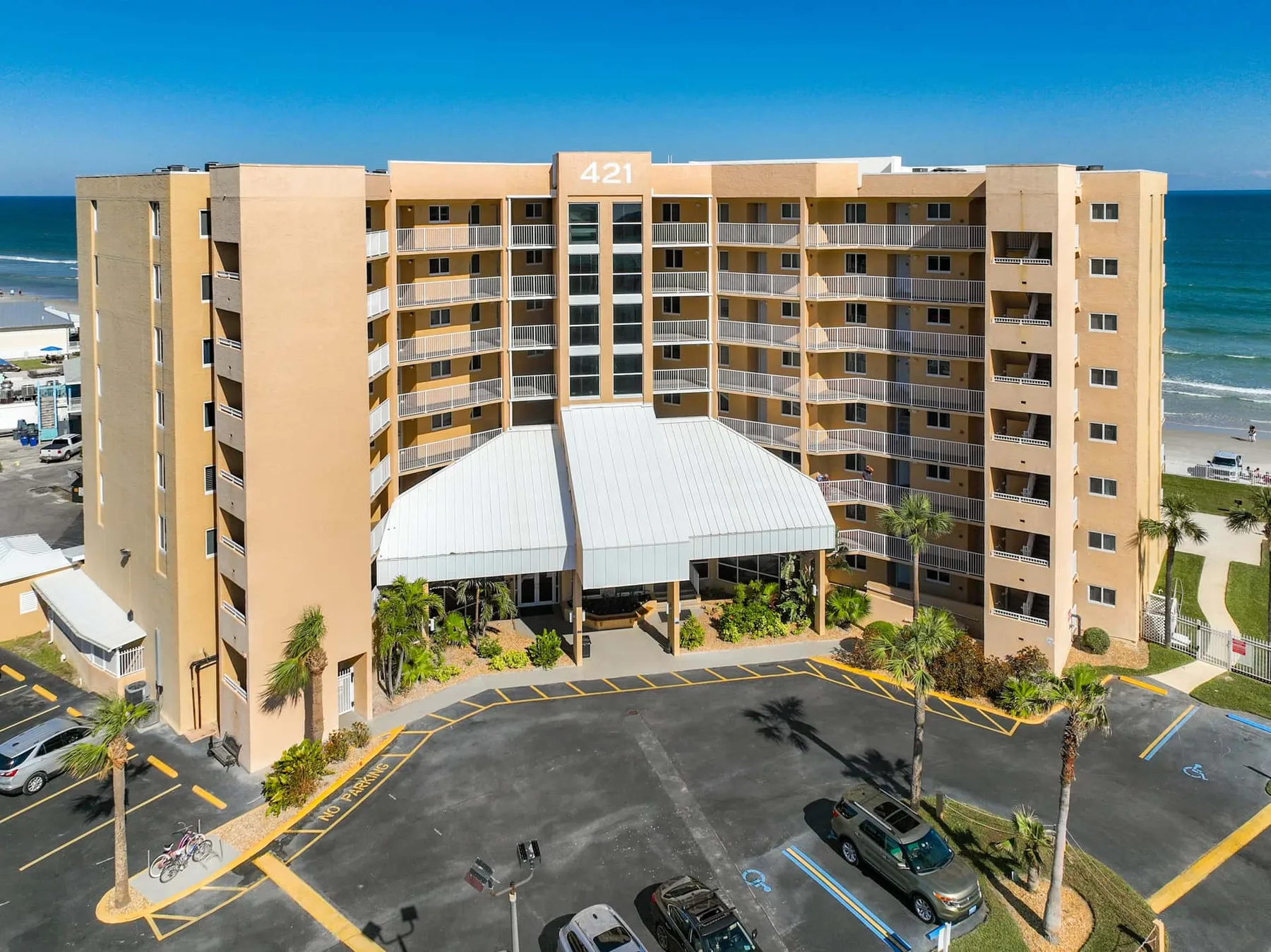 A beachfront multi-story building overlooks the ocean, with parking in front.