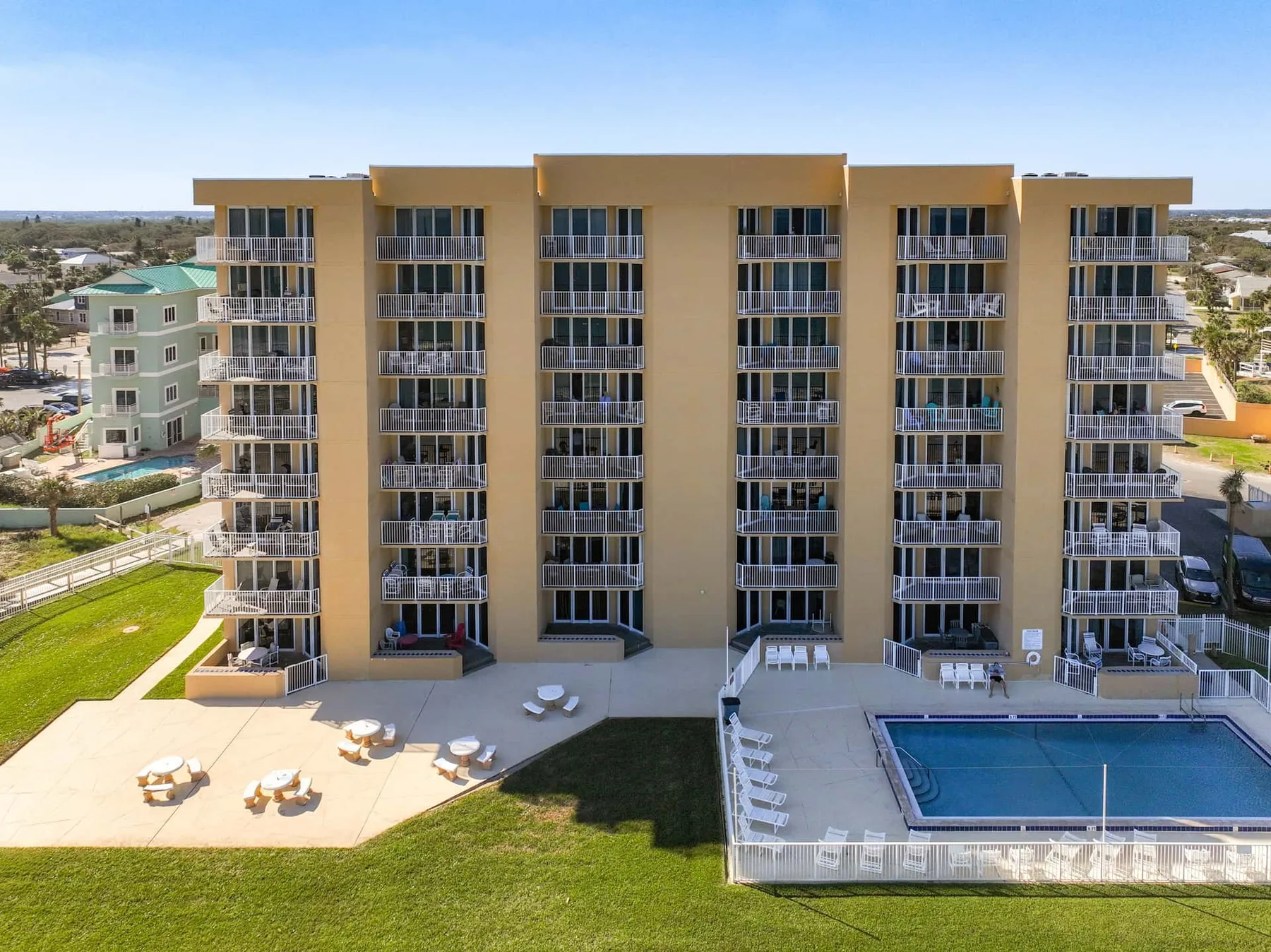 A multi-story building with balconies overlooks a pool and landscaped grounds.