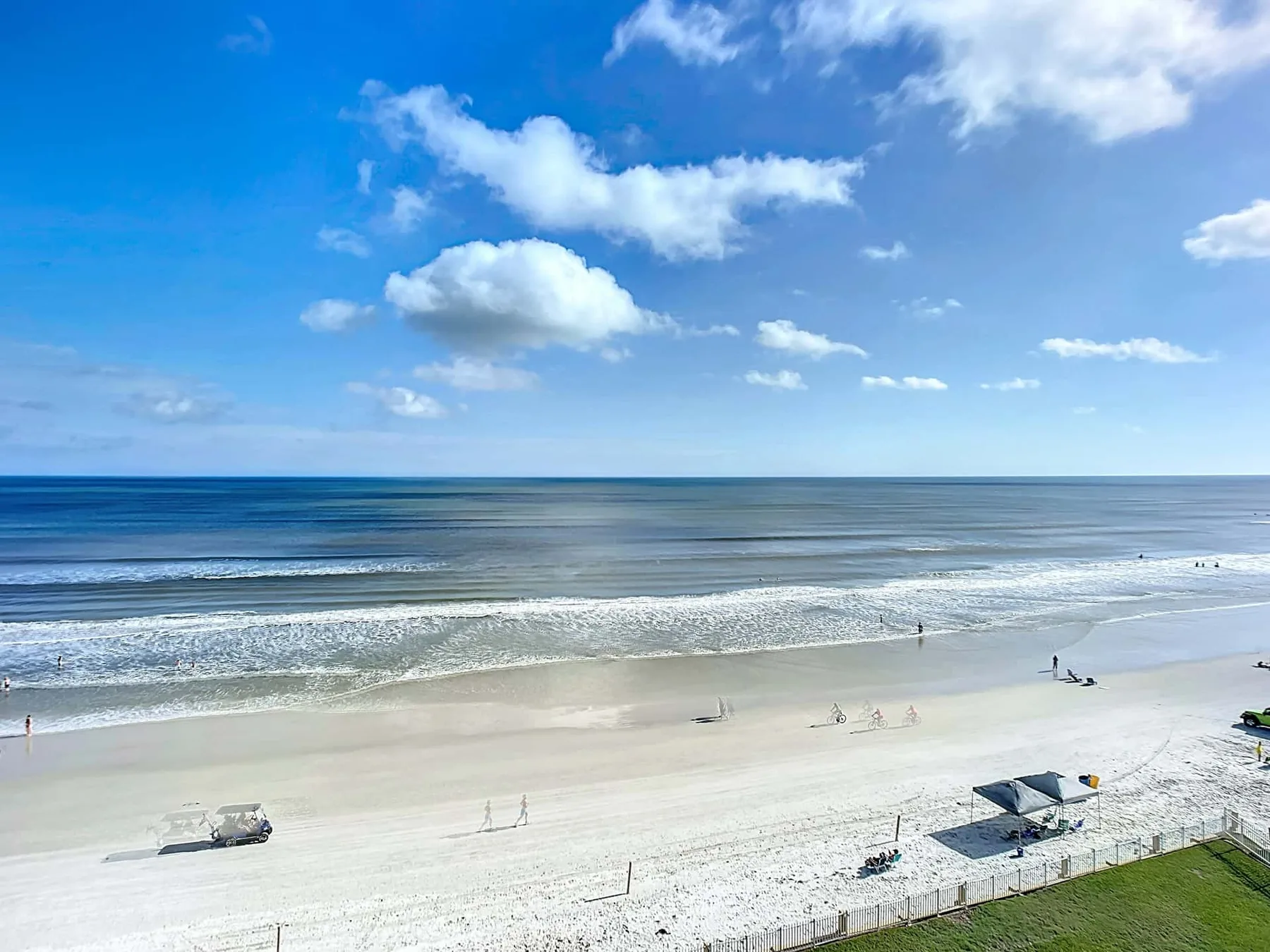 A sandy beach meets calm ocean waves beneath a partly cloudy sky.