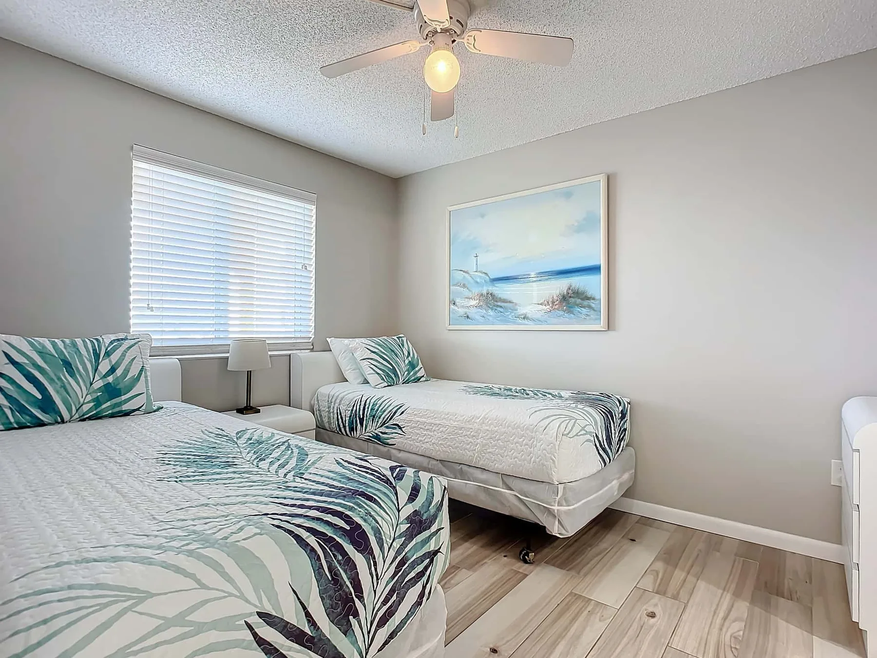 A bedroom with two beds, patterned bedding, and a window with blinds.