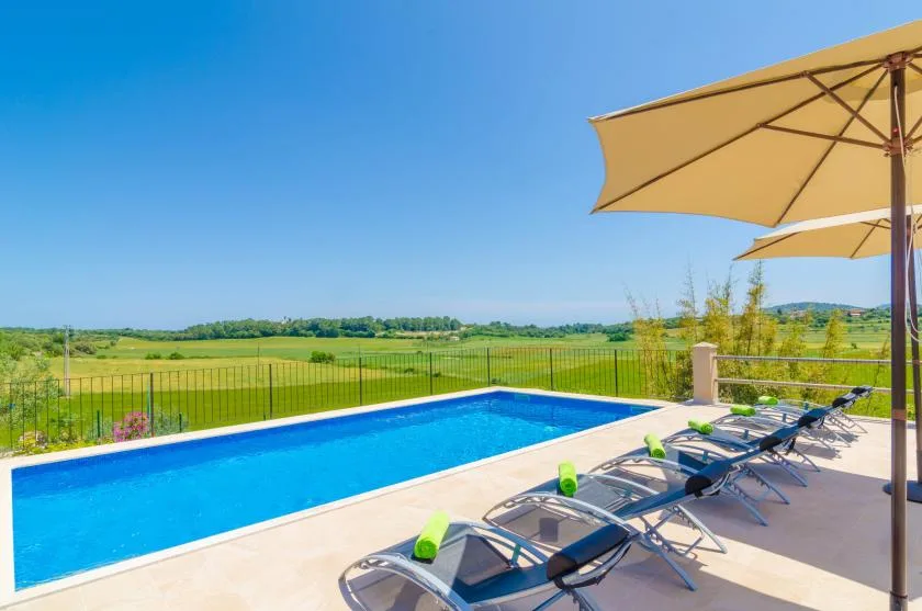 Una piscina al aire libre junto a asientos y sombrillas da a campos verdes.