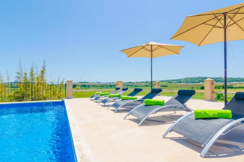 Una zona de asientos junto a la piscina exterior tiene tumbonas bajo sombrillas beige.