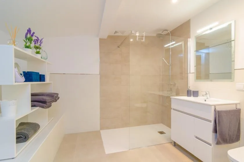 Un baño luminoso tiene una ducha a ras de suelo y un mueble de lavabo blanco.