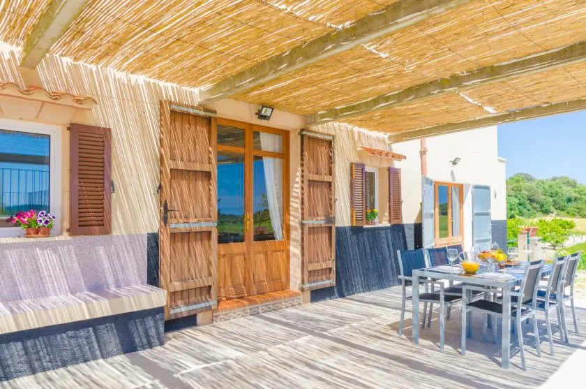 Una terraza de comedor a la sombra con una mesa de madera y sillas.