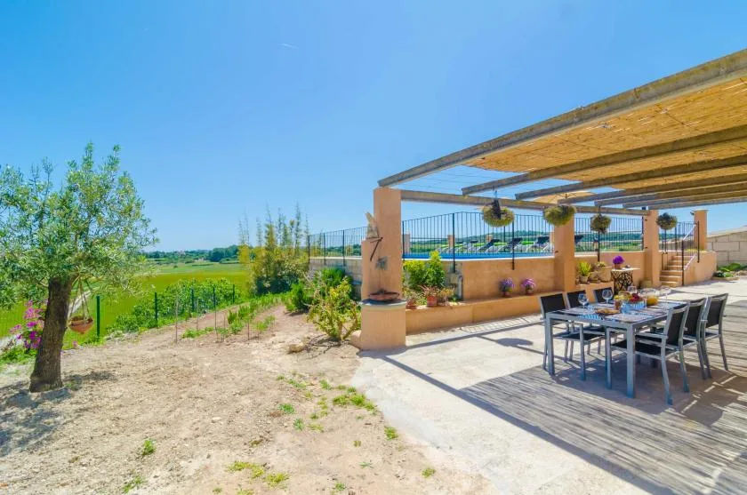 Una zona de comedor al aire libre está bajo una pérgola de madera junto a un campo abierto.