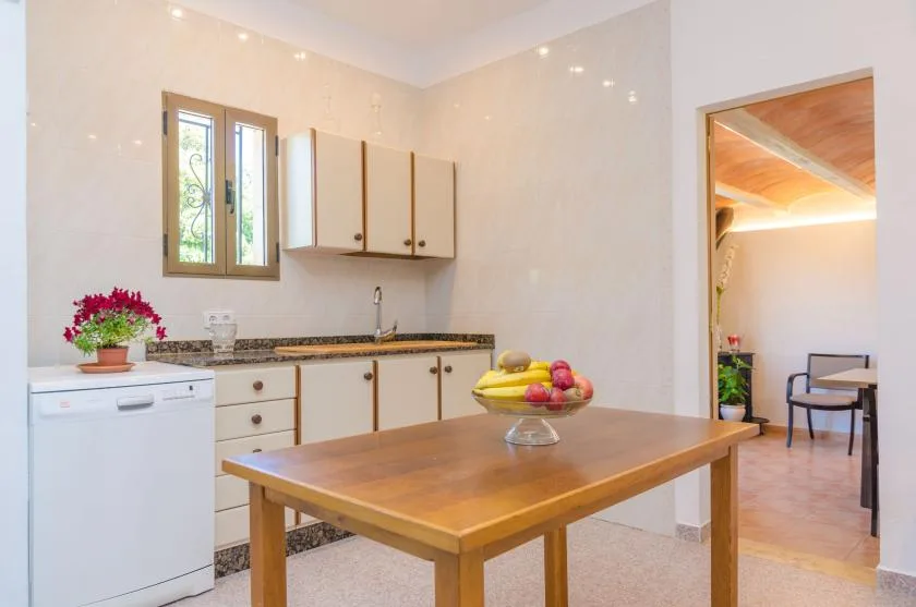 Una cocina luminosa con una mesa de madera, armarios y un fregadero pequeño.