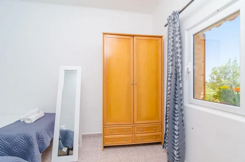 Un dormitorio con una cama, un armario y una ventana con vista a la vegetación.