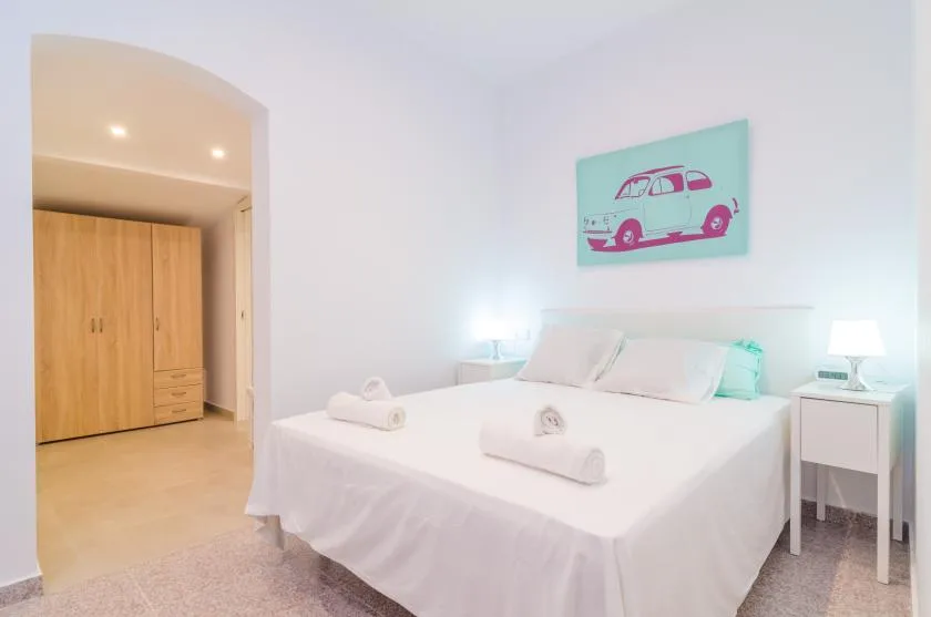 Un dormitorio luminoso con una cama tendida y una colorida ilustración de un vehículo en la pared.