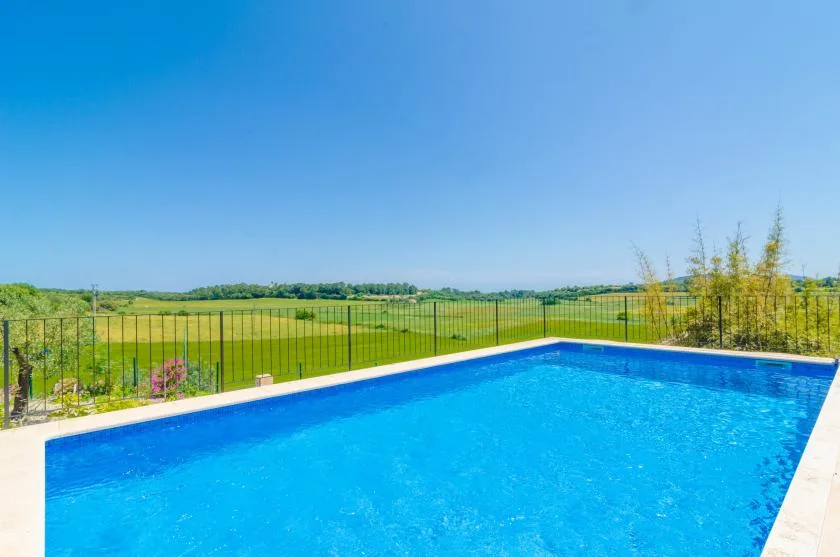 Una piscina al aire libre está junto a campos verdes bajo un cielo azul despejado.
