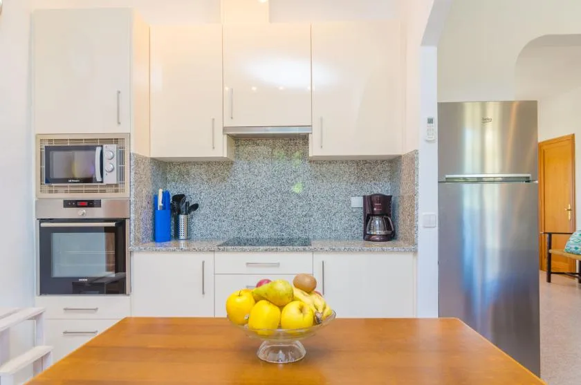 Una cocina luminosa con gabinetes blancos, un salpicadero estampado y fruta sobre la encimera.