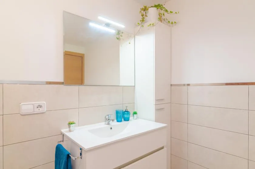 Un tocador de baño luminoso con lavabo, espejo y paredes de azulejos.