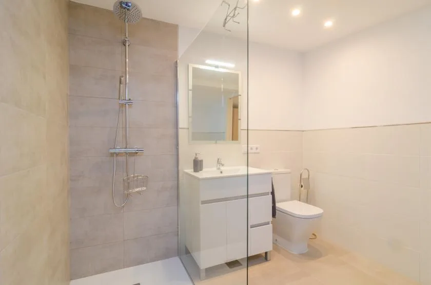 Un baño luminoso con ducha de vidrio, lavabo con mueble e inodoro.