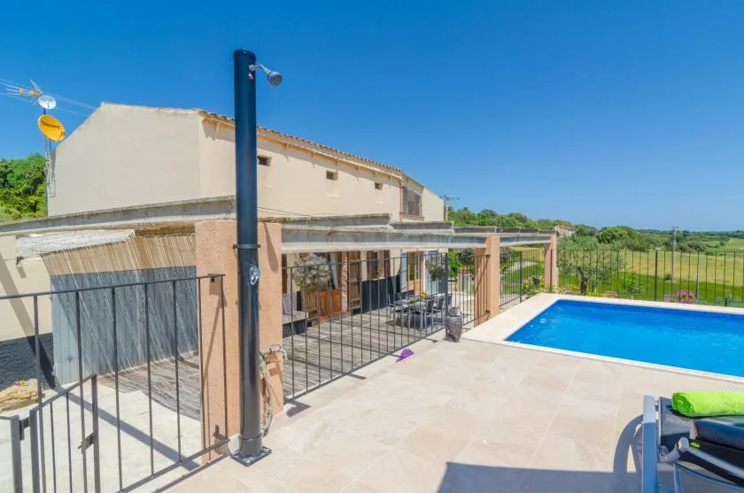 Una piscina y un patio pavimentado están junto a una casa con una zona de estar a la sombra.