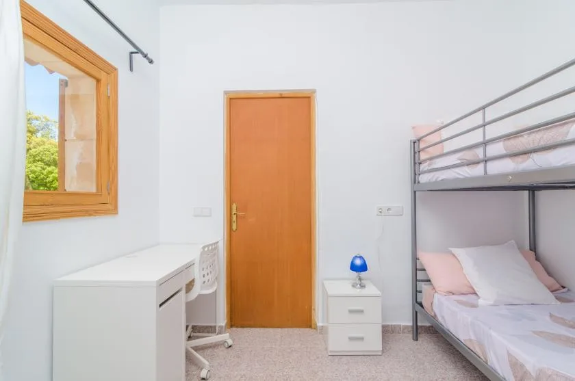 Un dormitorio luminoso con literas, un escritorio y una puerta de madera.