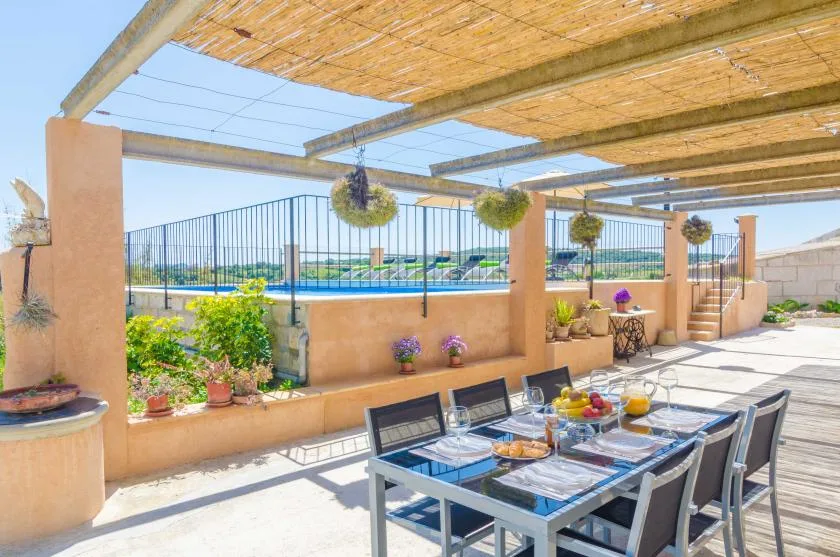 Una zona de comedor exterior a la sombra, con mesa y sillas junto a una piscina cercada.
