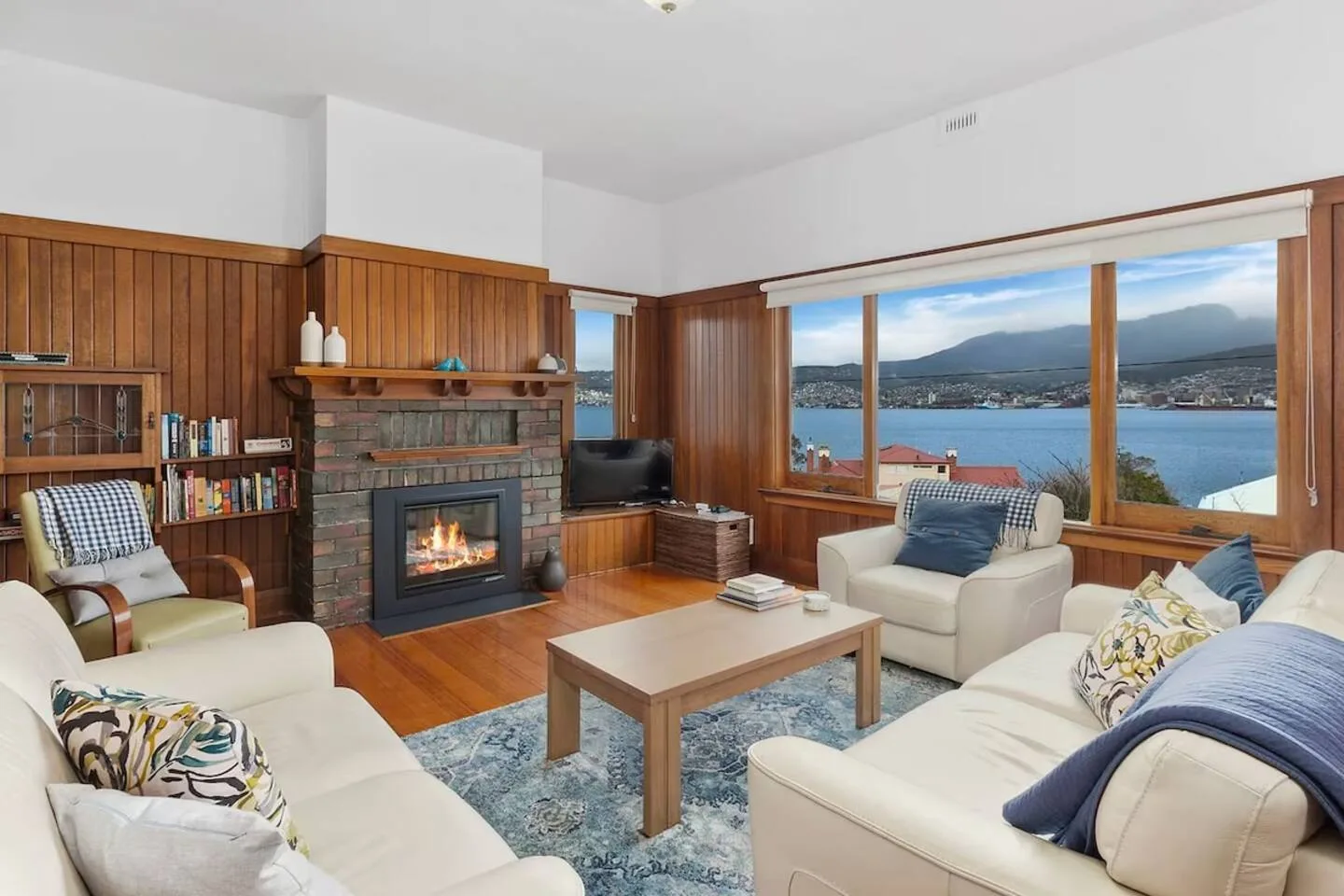 Sala de estar con asientos, una chimenea encendida y amplias ventanas con vistas al agua.