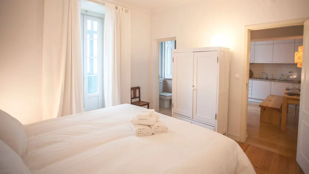 Un dormitorio con una cama junto a una ventana y una puerta abierta a la cocina.
