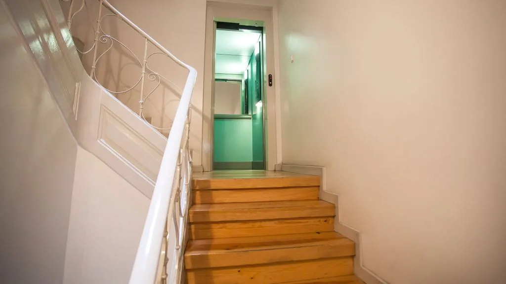 Una escalera de madera sube hasta una puerta con el interior iluminado de verde.