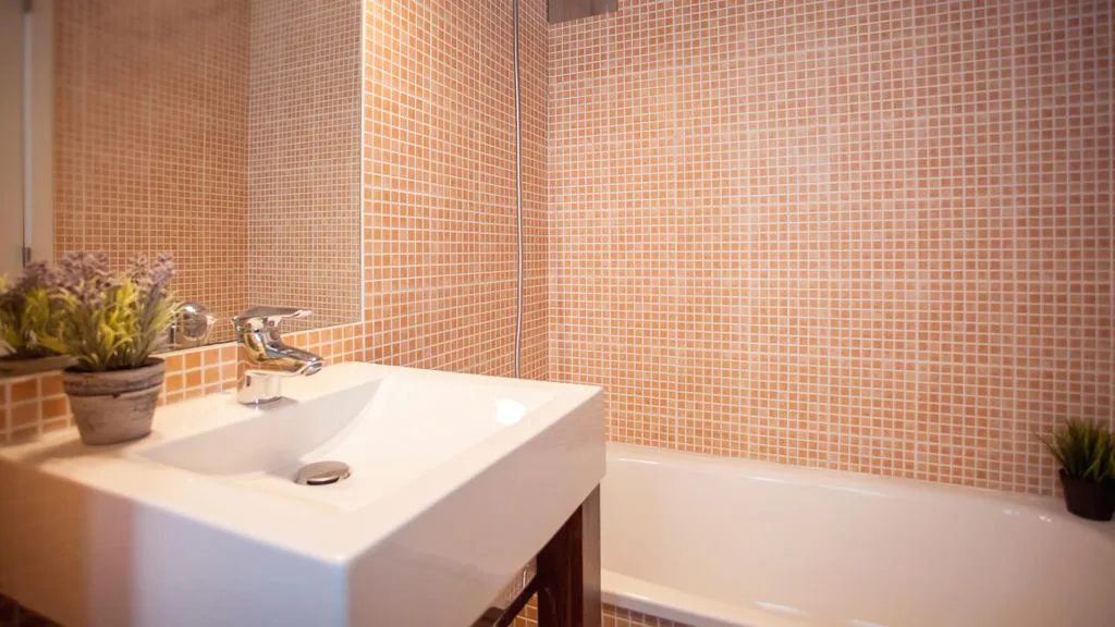 Un baño con lavabo blanco y bañera junto a paredes alicatadas.