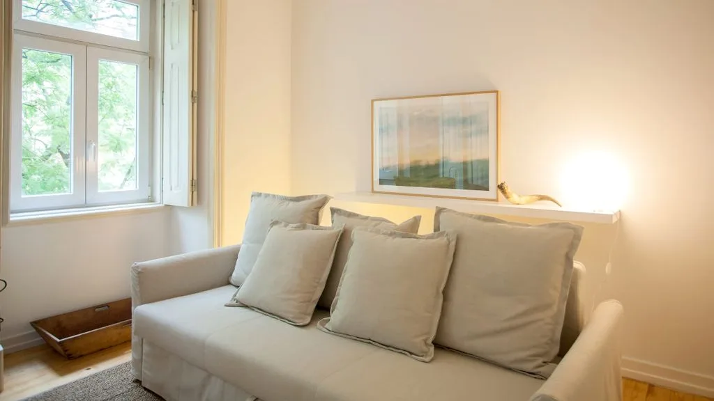 Una sala de estar luminosa con un sofá beige bajo un cuadro enmarcado.