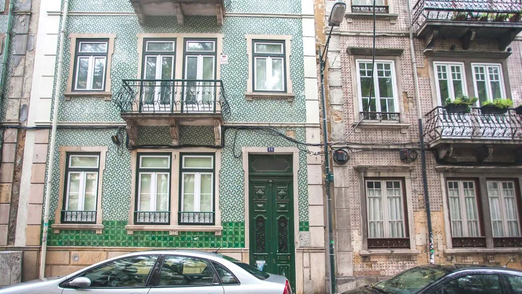 Una calle urbana con fachadas de apartamentos revestidas de azulejos y coches aparcados.
