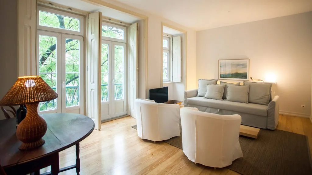 Una sala de estar con asientos alrededor de una alfombra junto a ventanas altas.