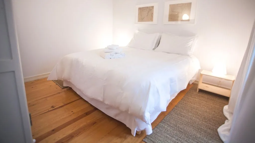 Un dormitorio con una cama blanca y cuadros enmarcados encima.