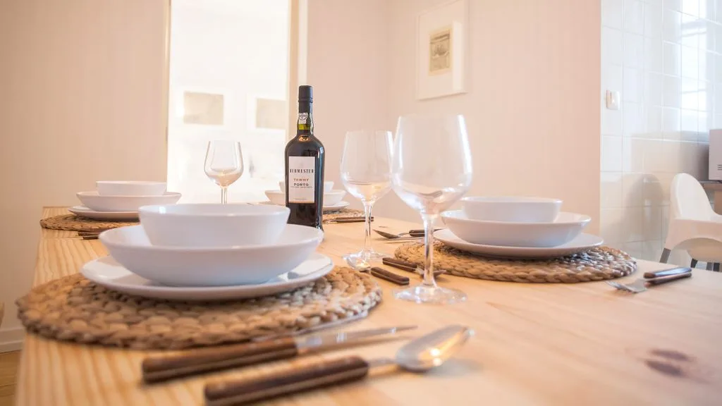 Una mesa de comedor está puesta con platos, copas y una botella de vino.