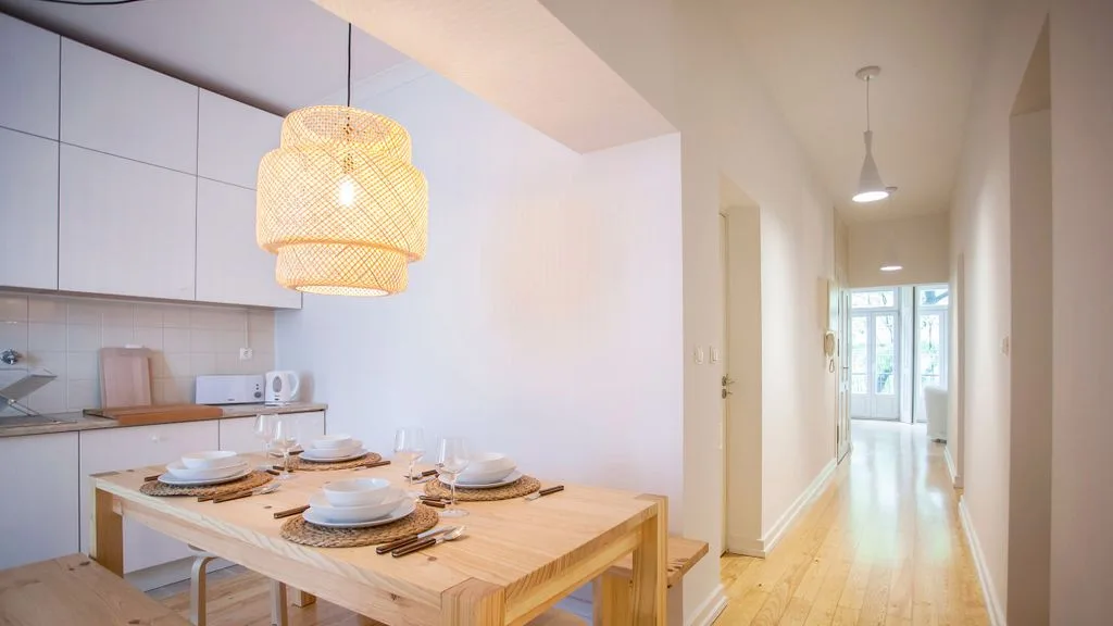 Comedor abierto con una mesa de madera junto a una cocina compacta y un pasillo.