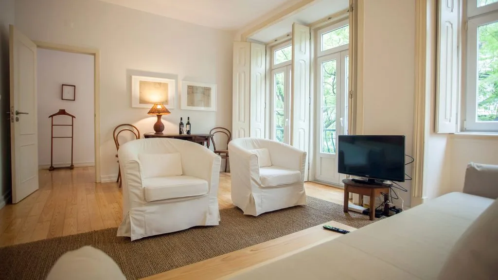 Una sala de estar luminosa con asientos, un televisor y ventanas altas.