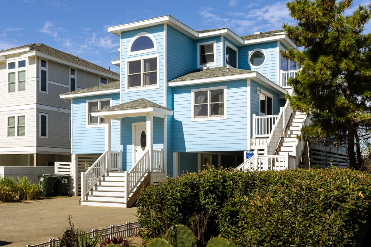 Una casa azul de varios niveles con molduras blancas, escaleras exteriores y arbustos alrededor.