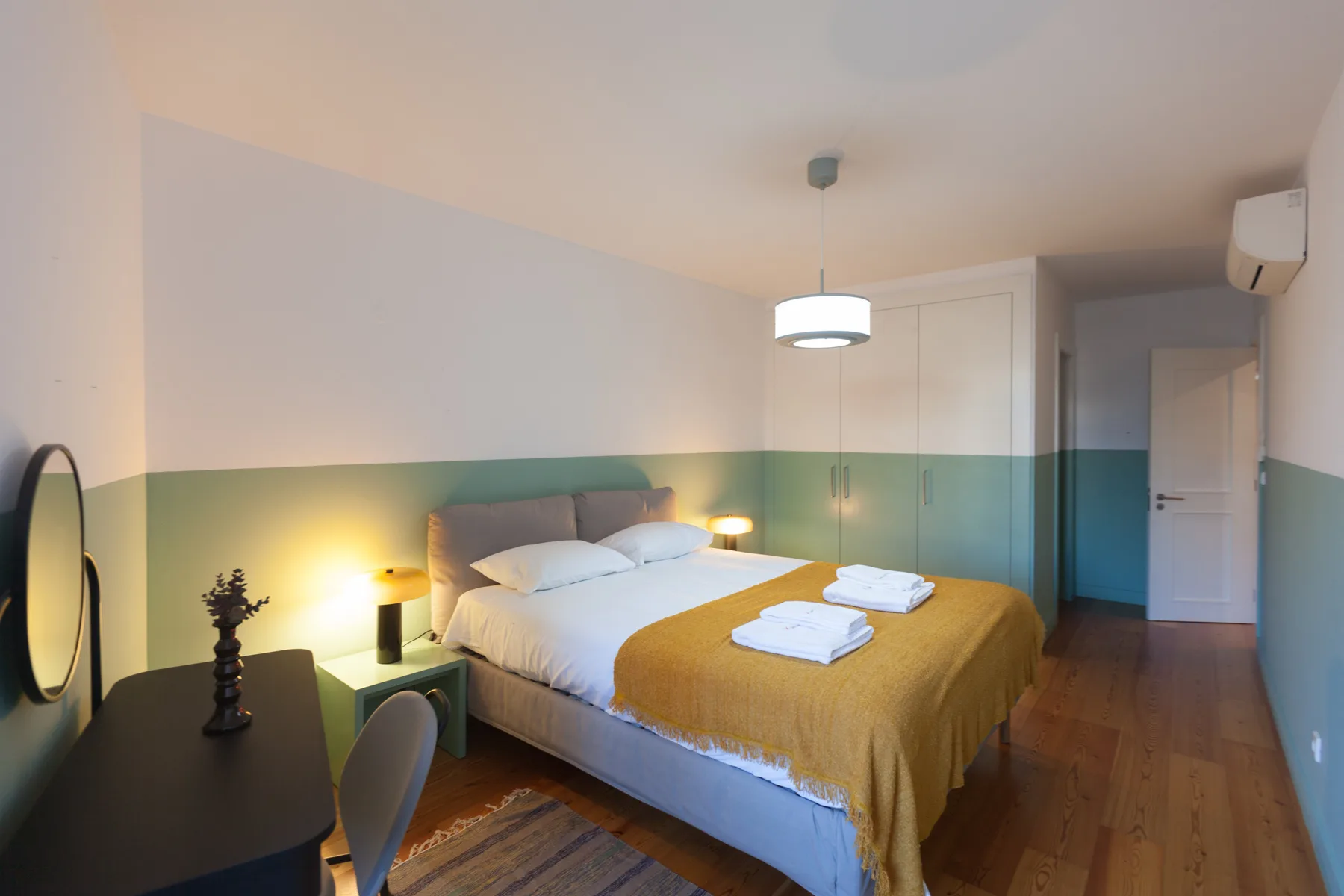 A bedroom with a double bed, bedside lamps, and a mustard-colored coverlet.