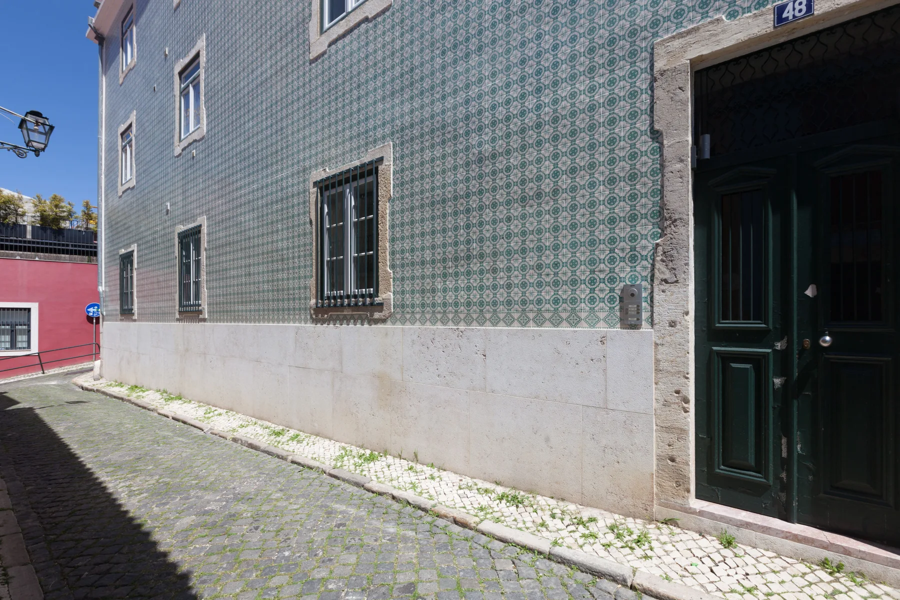A cobblestone street runs alongside a tiled building facade and dark entrance.