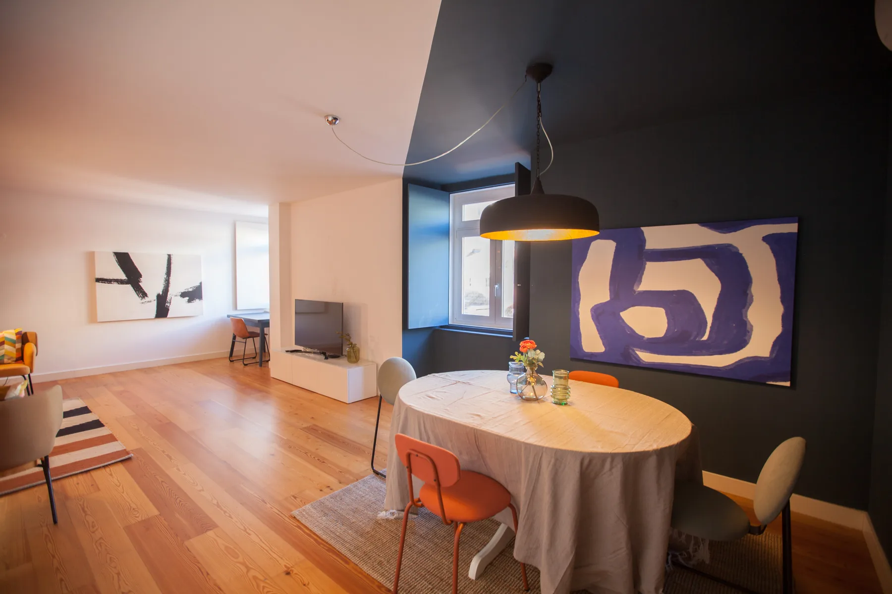 A dining area with a round table and colorful abstract artwork beside a living space.