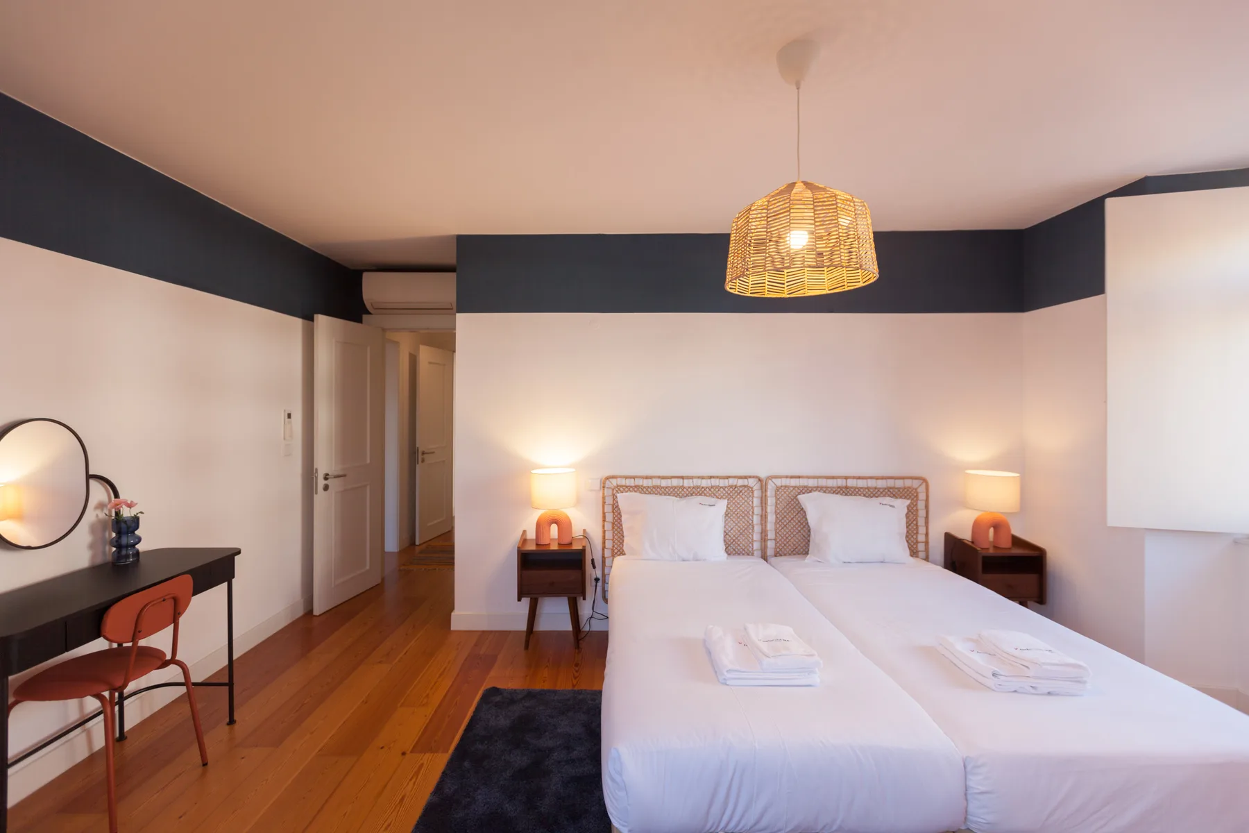A bedroom with two beds, bedside tables, and a desk along the wall.
