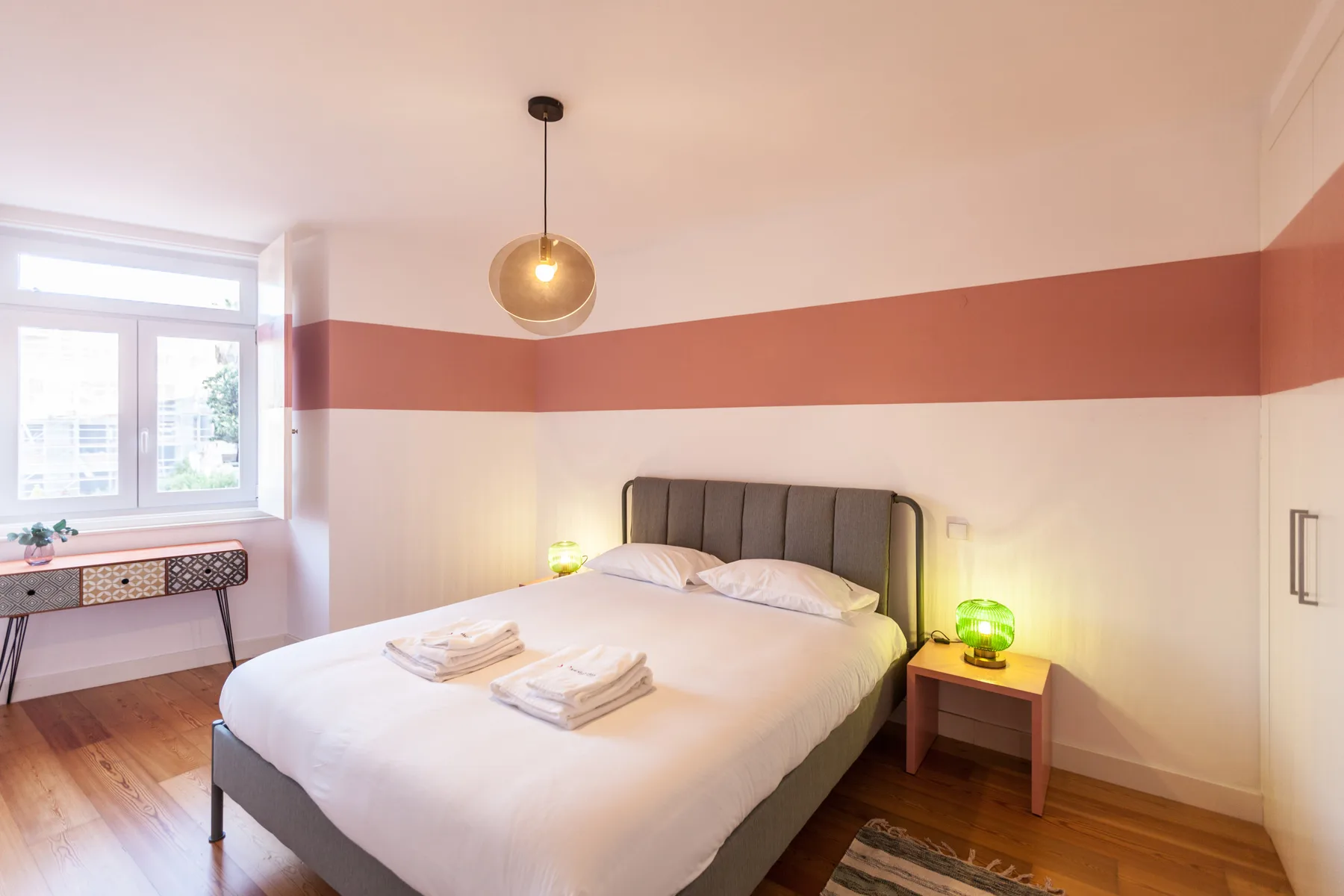 A bedroom with a neatly made bed and a window beside it.