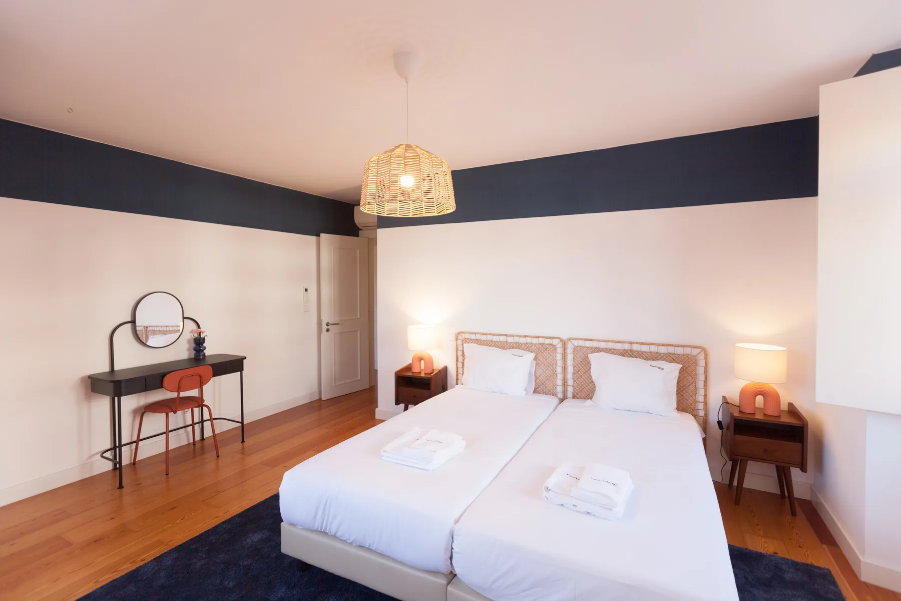 A bedroom with two beds, bedside tables, and a small desk.