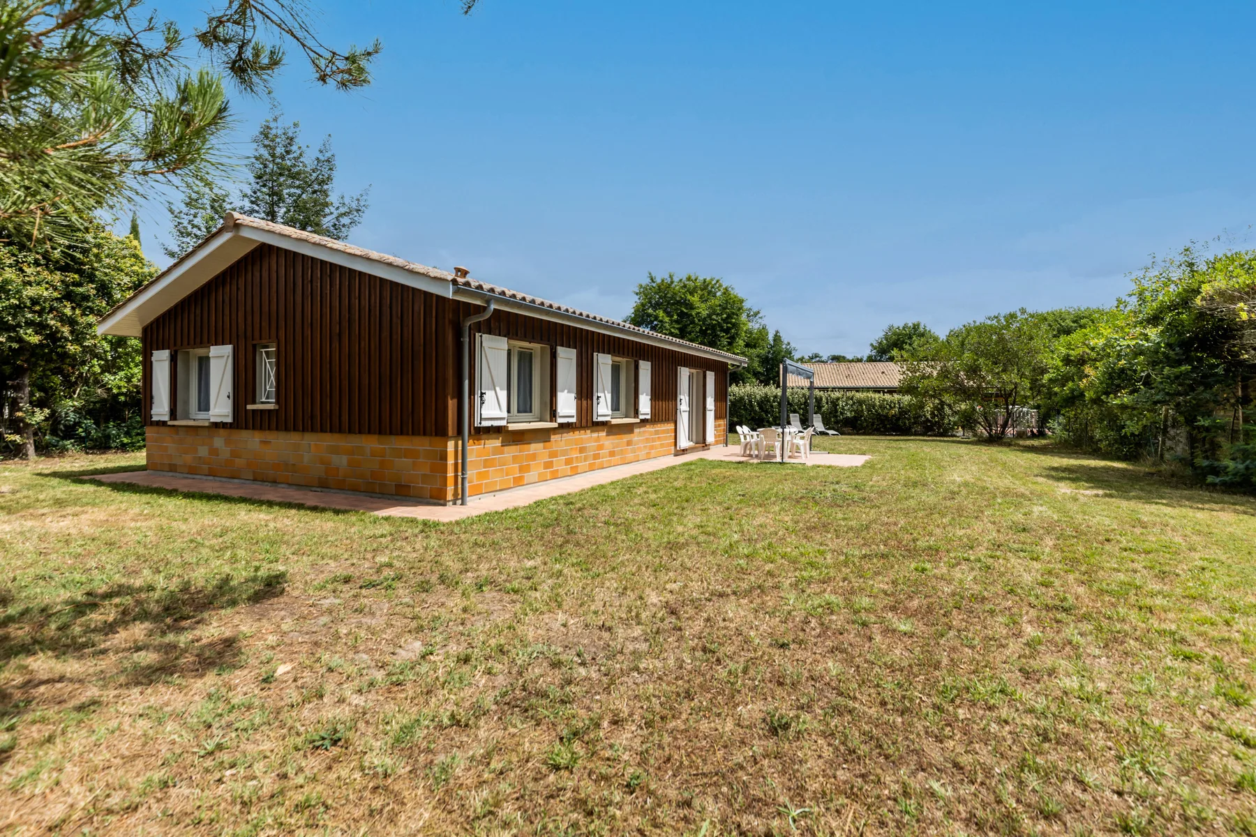 A single-story house stands beside a broad grassy yard under a clear sky.