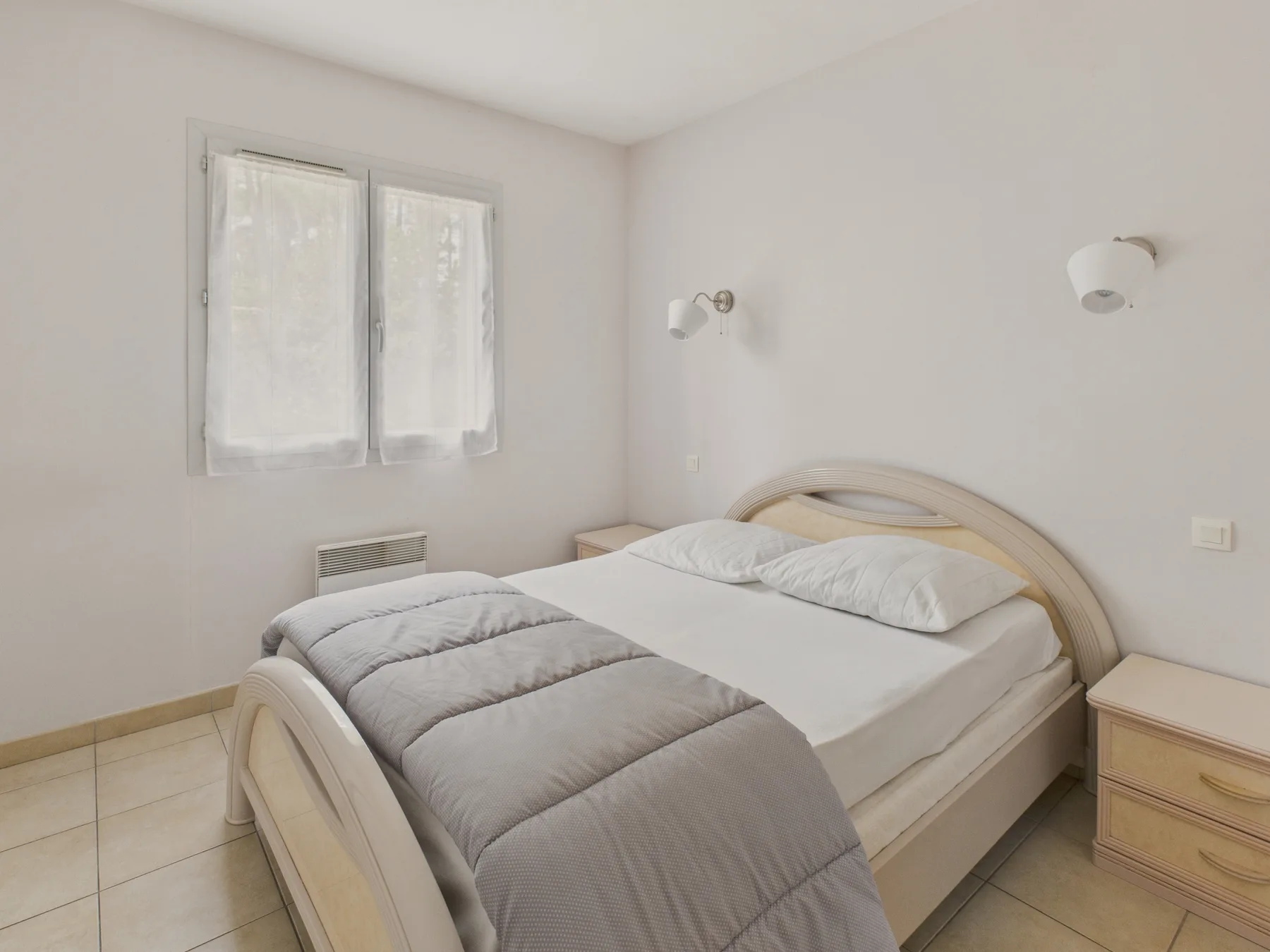 A bedroom with a double bed, light bedding, and a curtained window.