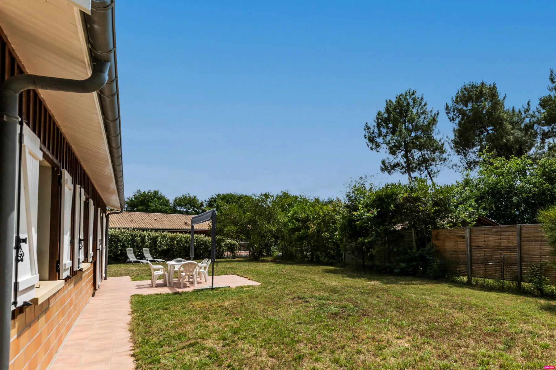 A house exterior opens onto a grassy yard with outdoor seating.