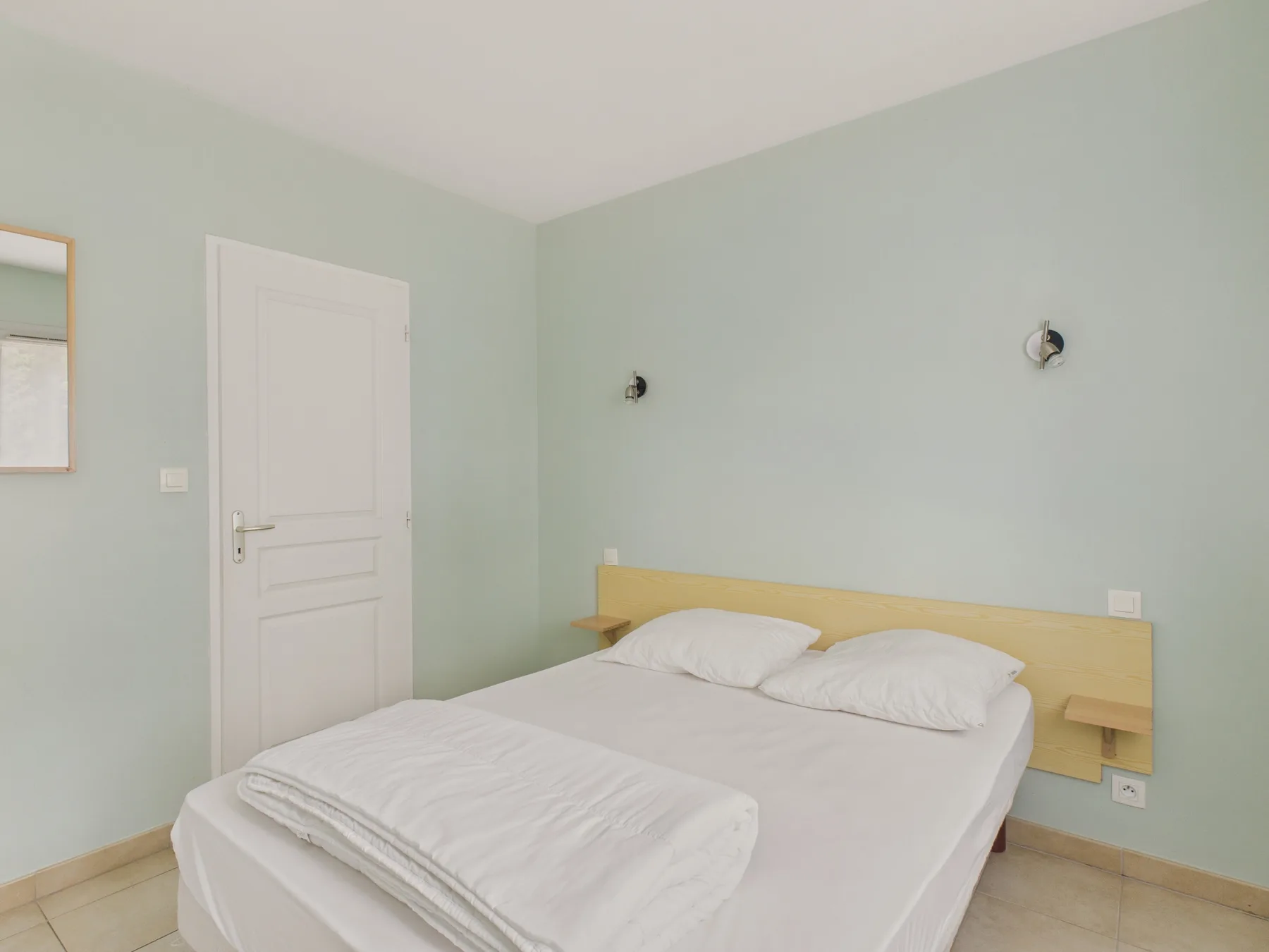 A bedroom with a neatly made bed and pale green walls.