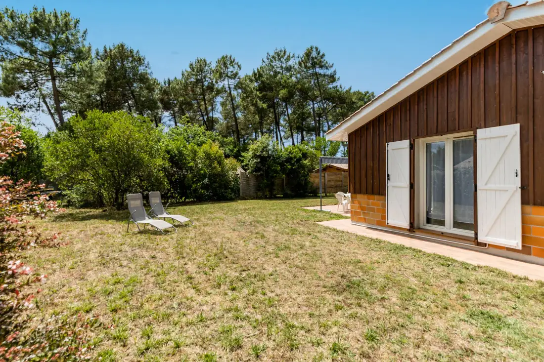 A house beside a grassy yard with outdoor seating and trees.