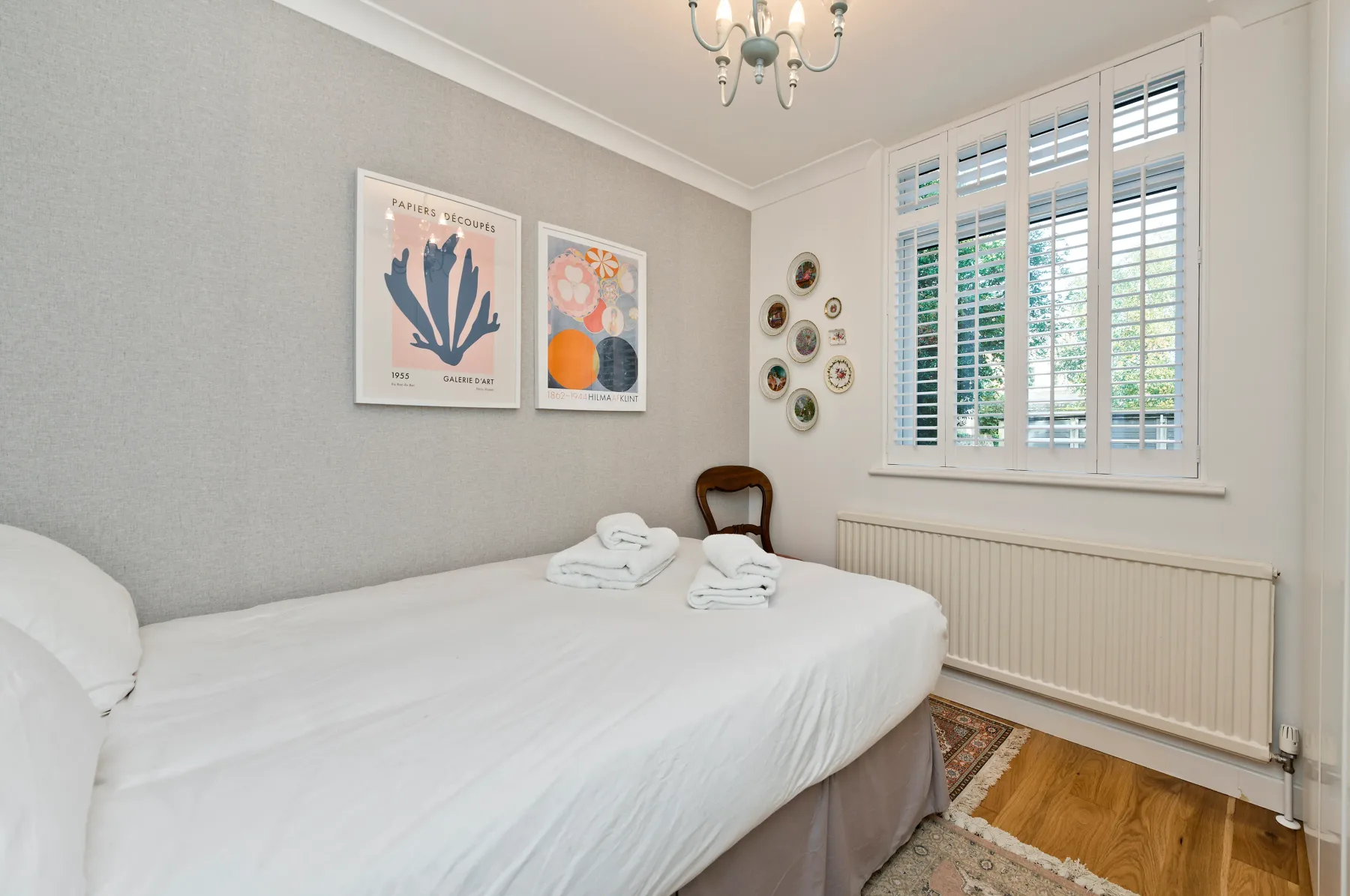 A bedroom with a neatly made bed beneath framed botanical prints.