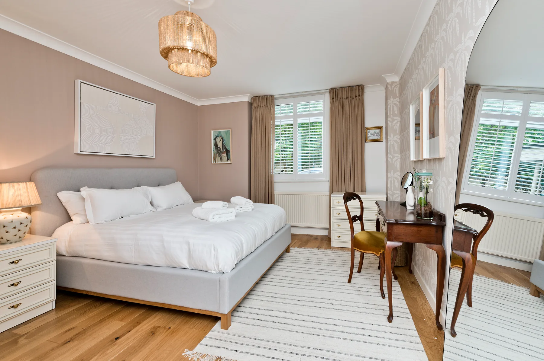 A bright bedroom with a neatly made bed, a desk, and a large mirror.
