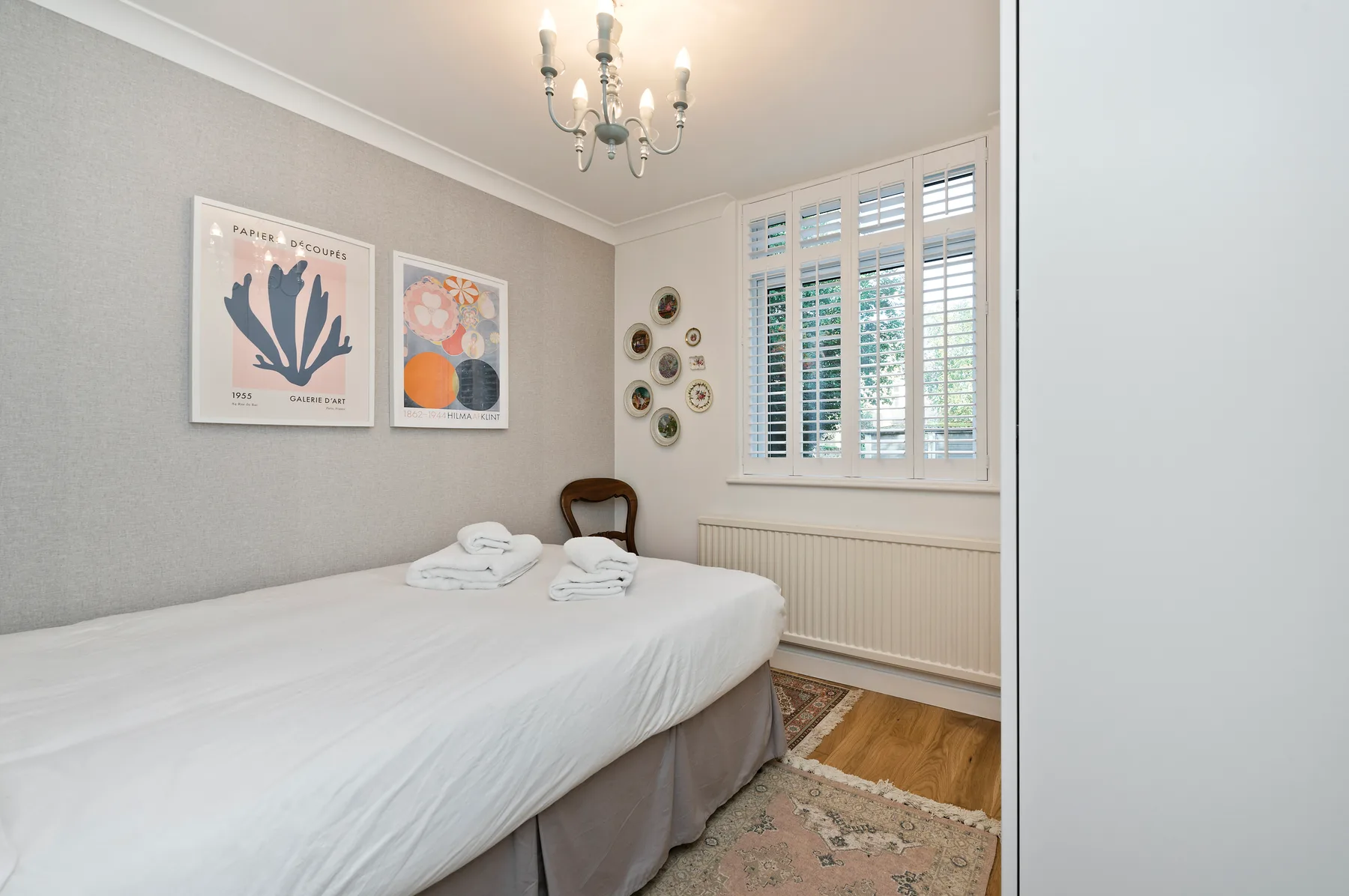 A bright bedroom with a neatly made bed and shuttered windows.
