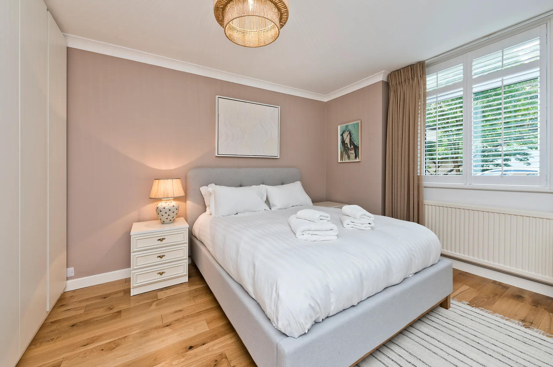 A bedroom with a neatly made bed, bedside table, and large window.