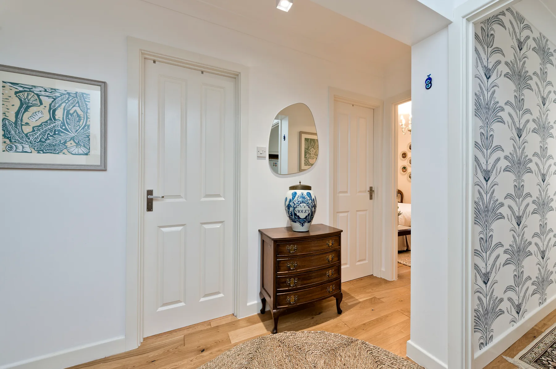 A bright hallway with white paneled doors, a small dresser, and framed artwork.