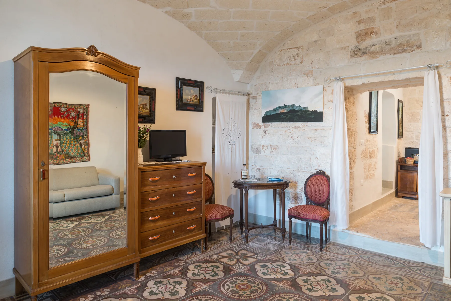A furnished bedroom with a mirrored wardrobe, dresser, and small table.