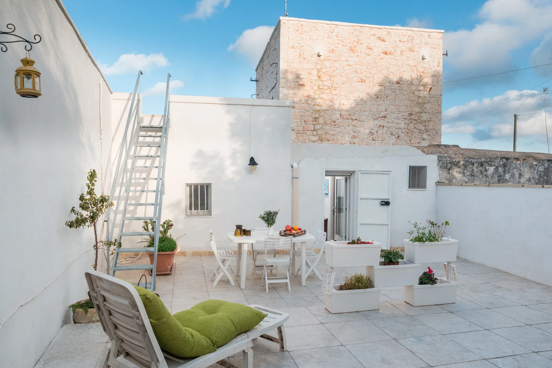 A bright rooftop terrace with white seating, potted plants, and a table.
