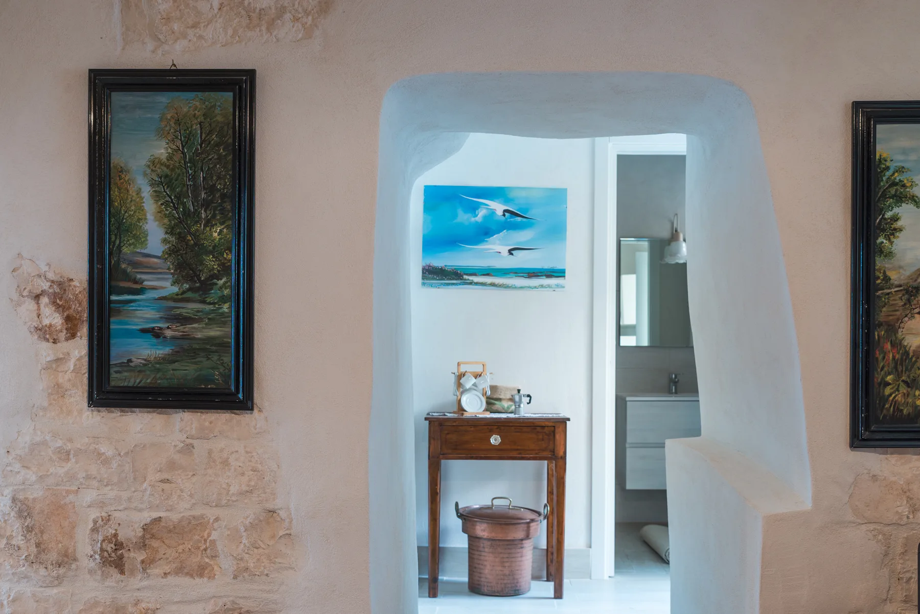 A pale interior wall frames an arched opening to a bright room with a small wooden table.
